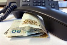 słuchawka telefonu leży na stoliku przy niej banknoty pieniędzy, w tle telefon z klawiaturą