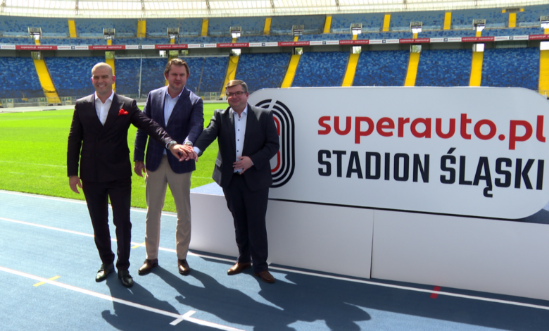 Stadion Śląski nowa nazwa Trzech mężczyzn na bieżni stadionu trzyma się za rękę. w tle duży napis