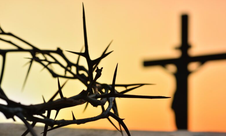 Wielki piątek, na pierwszym planie korona cierniowa w tle rozmazany krzyż na tle nieba w promieniach zachodzącego słońca