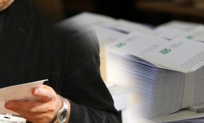 Dodatkowa emerytura - grafika, fragment postaci, ręce trzymające dokument w tle stosy kopert z listami do doręczenia