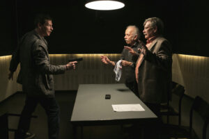 kadr z filmu Emeryci na Tropie trzech mężczyzn. Jeden mierzy z pistoletu do pozostałej dwójki 