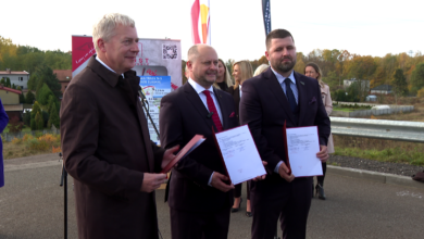 Trasa N-s Trzech mężczyzn trzyma w rękach papierowe teczki pozuja do zdjęcia w tle kolorowe flagi i stojący ludzie