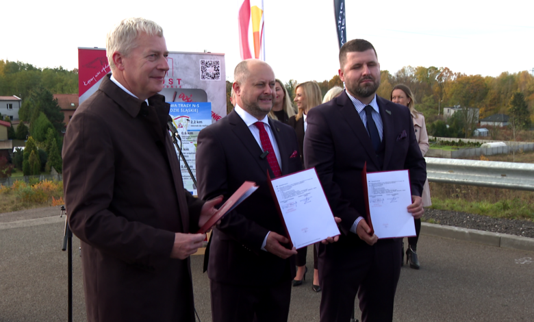 Trasa N-s Trzech mężczyzn trzyma w rękach papierowe teczki pozuja do zdjęcia w tle kolorowe flagi i stojący ludzie