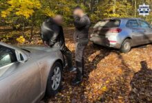 zATRZYMANY ZE SKRĘPOANYMI RĘKOMA Z TYŁU OPIERA SIĘ O MASKĘ SAMOCHODU OBOK STOI POLICJANT